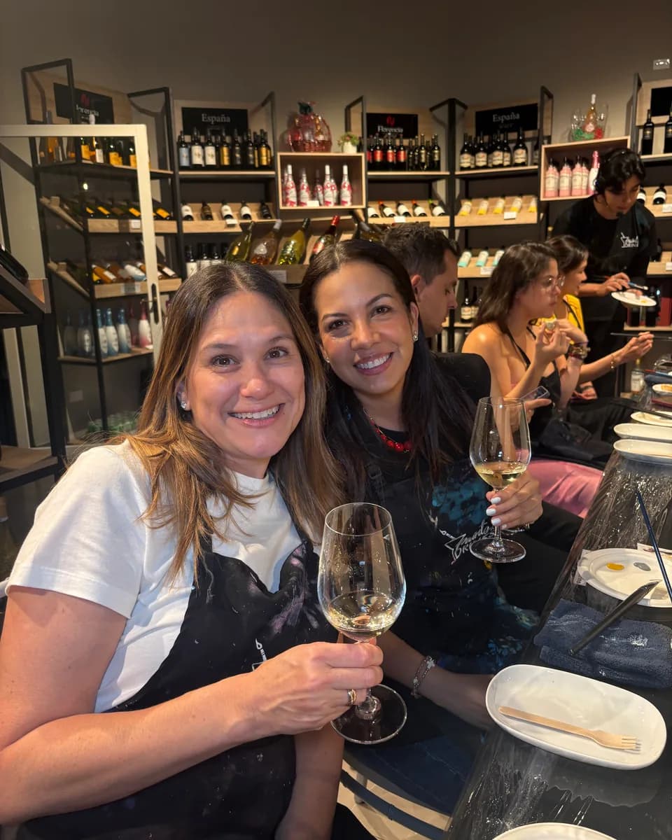 Two friends toast with wine in front of their canvases at an Artistic Pairing in a wine shop