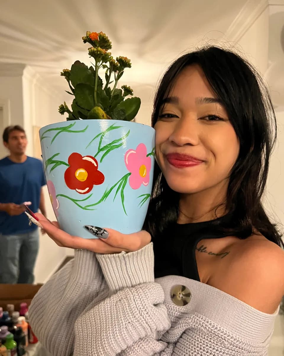 Participant smiles with her hand-painted flowerpot with red flowers and its plant